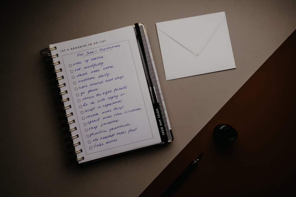 A neatly arranged stationery set with a to-do list, notebook, and envelope on a desk.