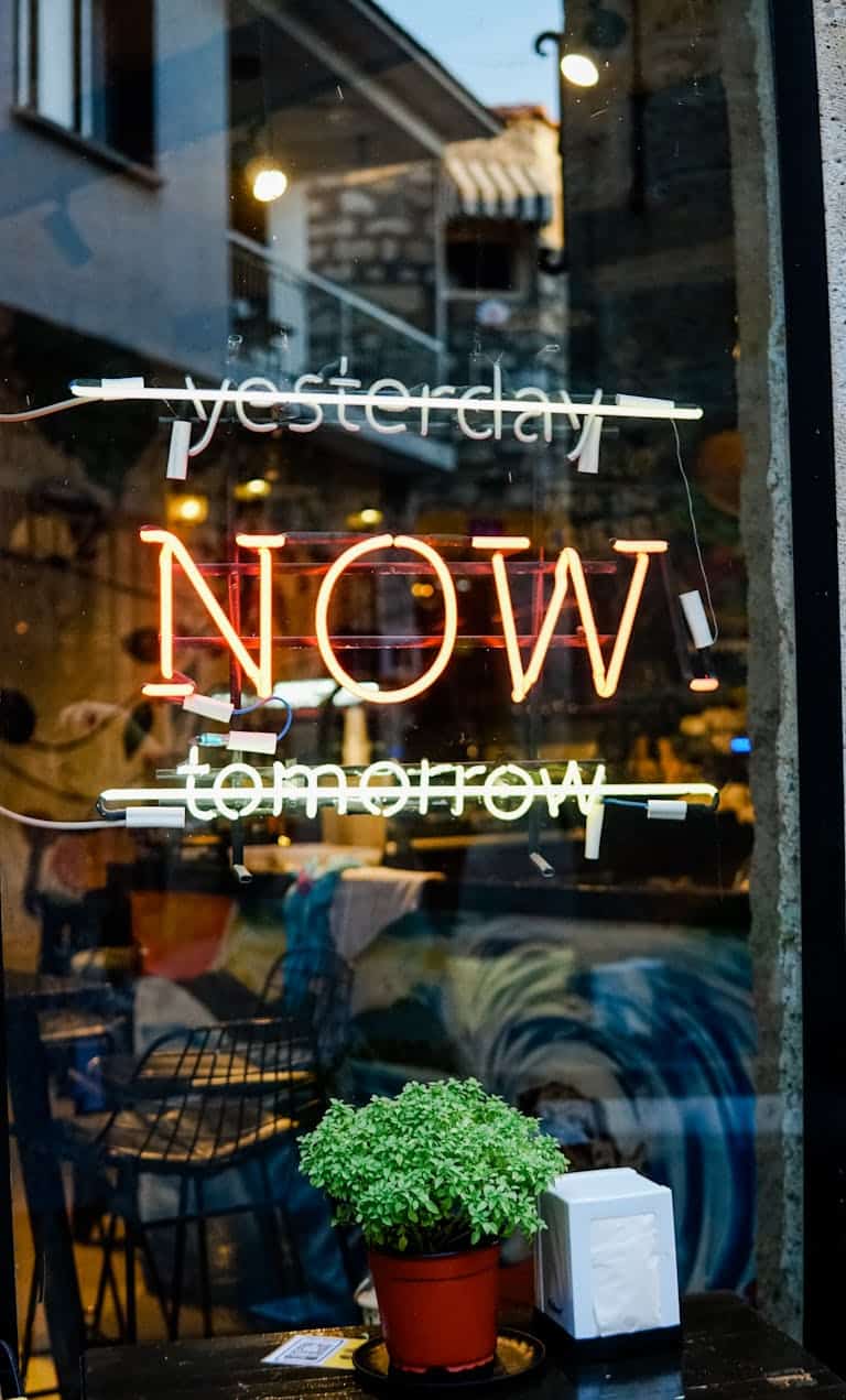 A colorful neon sign on a glass storefront with "Yesterday" and "Tomorrow" crossed out, leaving "Today" in the middle.