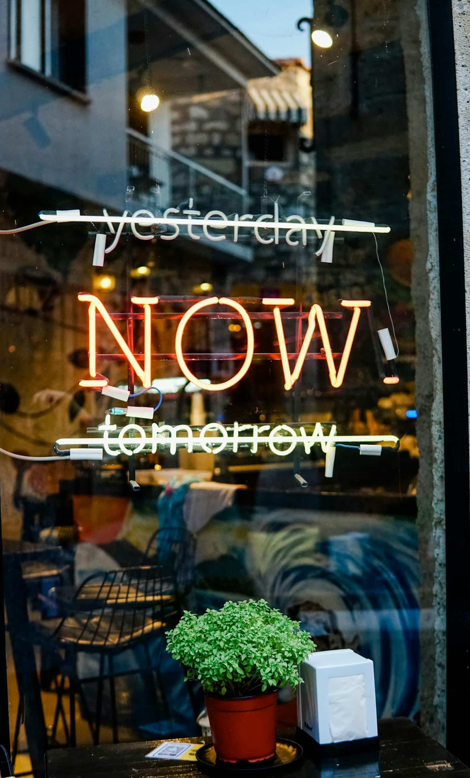 A colorful neon sign on a glass storefront with "Yesterday" and "Tomorrow" crossed out, leaving "Today" in the middle.