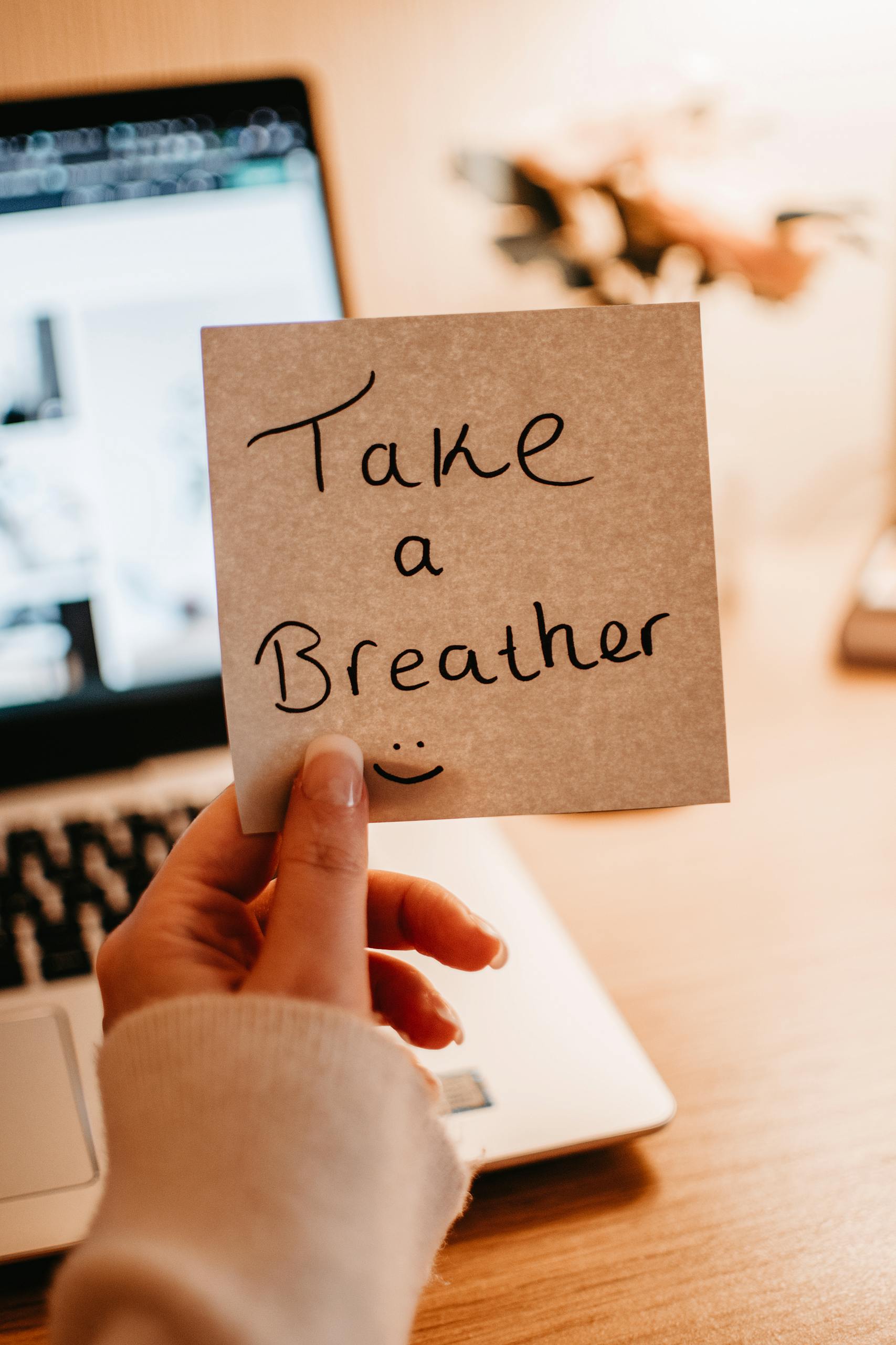 Hand holding a motivational note in a cozy home office setting.