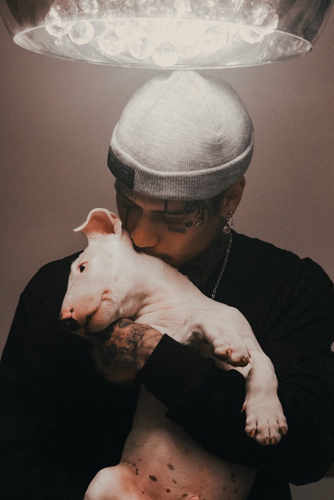 A tattooed man lovingly hugs a bull terrier puppy, showcasing affection and companionship.