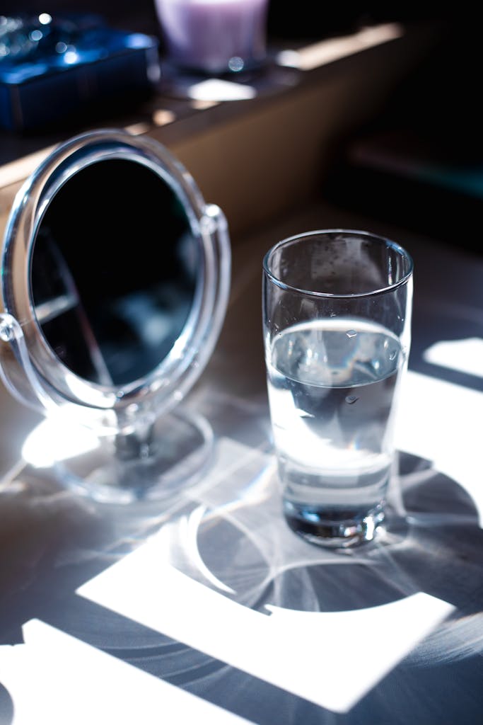 Glass of water casting reflections alongside a mirror on a bright sunny day.