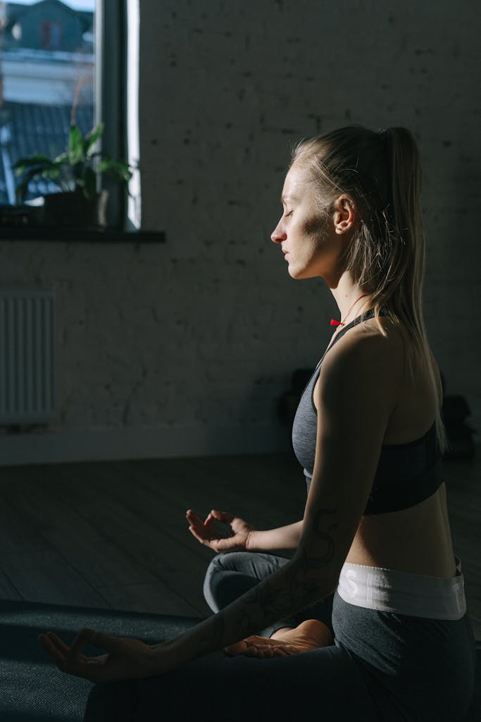 A woman is meditating indoors in a peaceful setting, focusing on mindfulness and serenity.