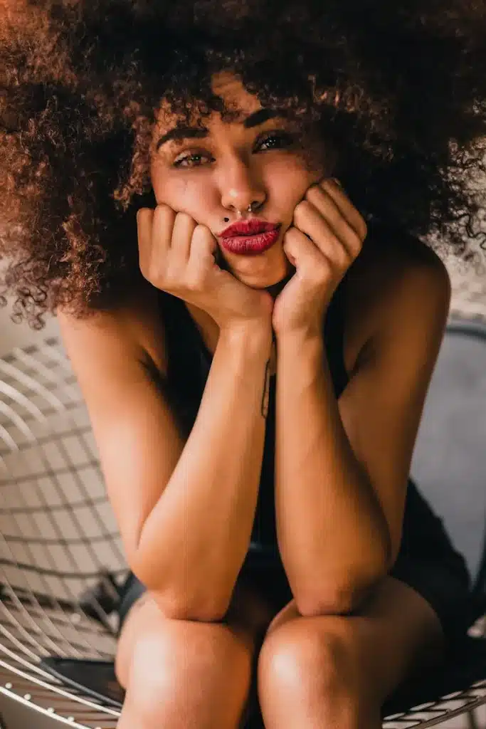 Portrait of a thoughtful woman with natural hair resting her face in her hands, expressing quiet reflection and emotional depth