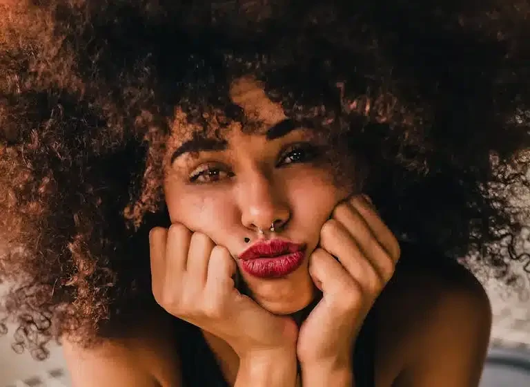 Portrait of a thoughtful woman with natural hair resting her face in her hands, expressing quiet reflection and emotional depth
