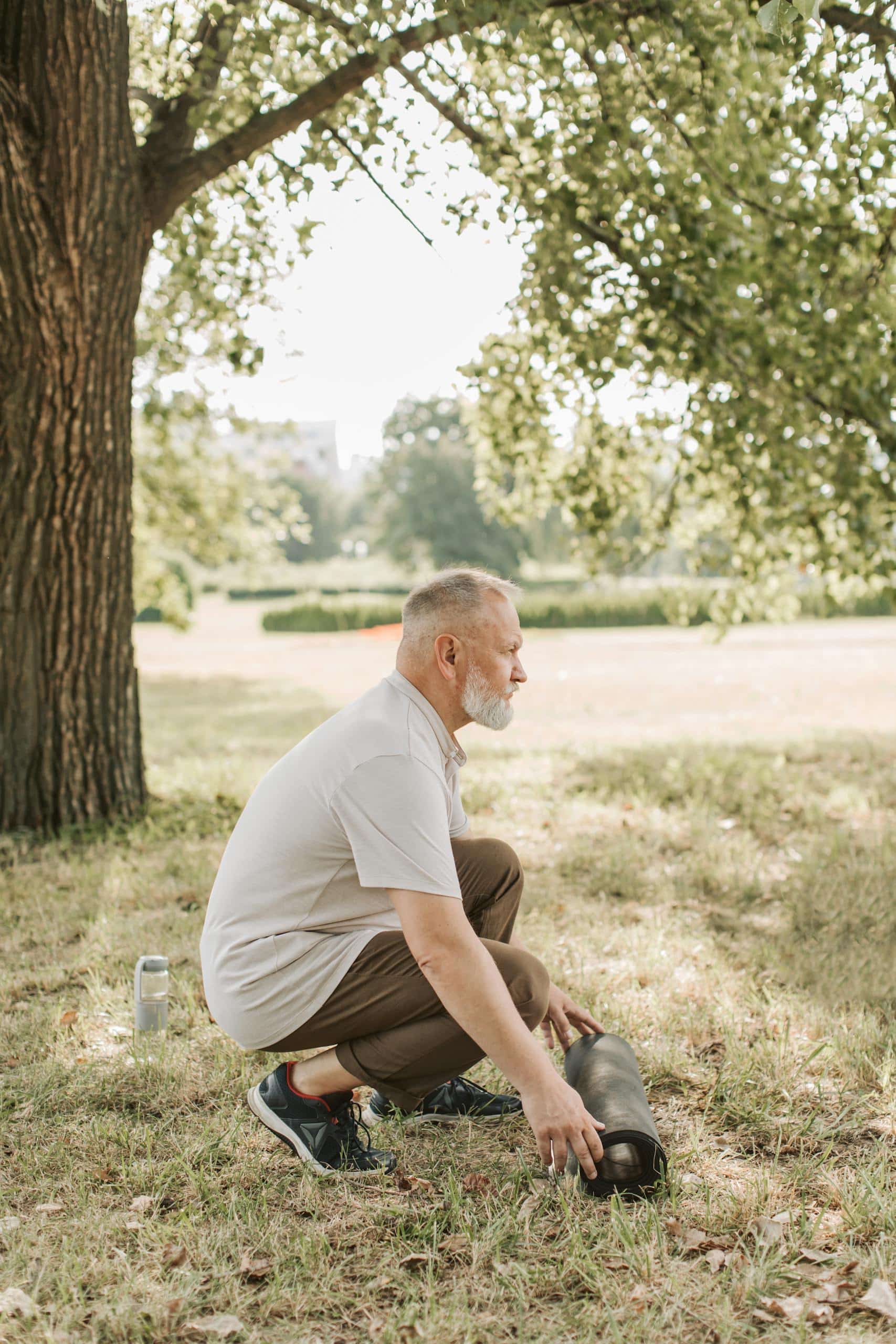 Senior man setting up yoga mat outdoors, promoting healthy lifestyle.